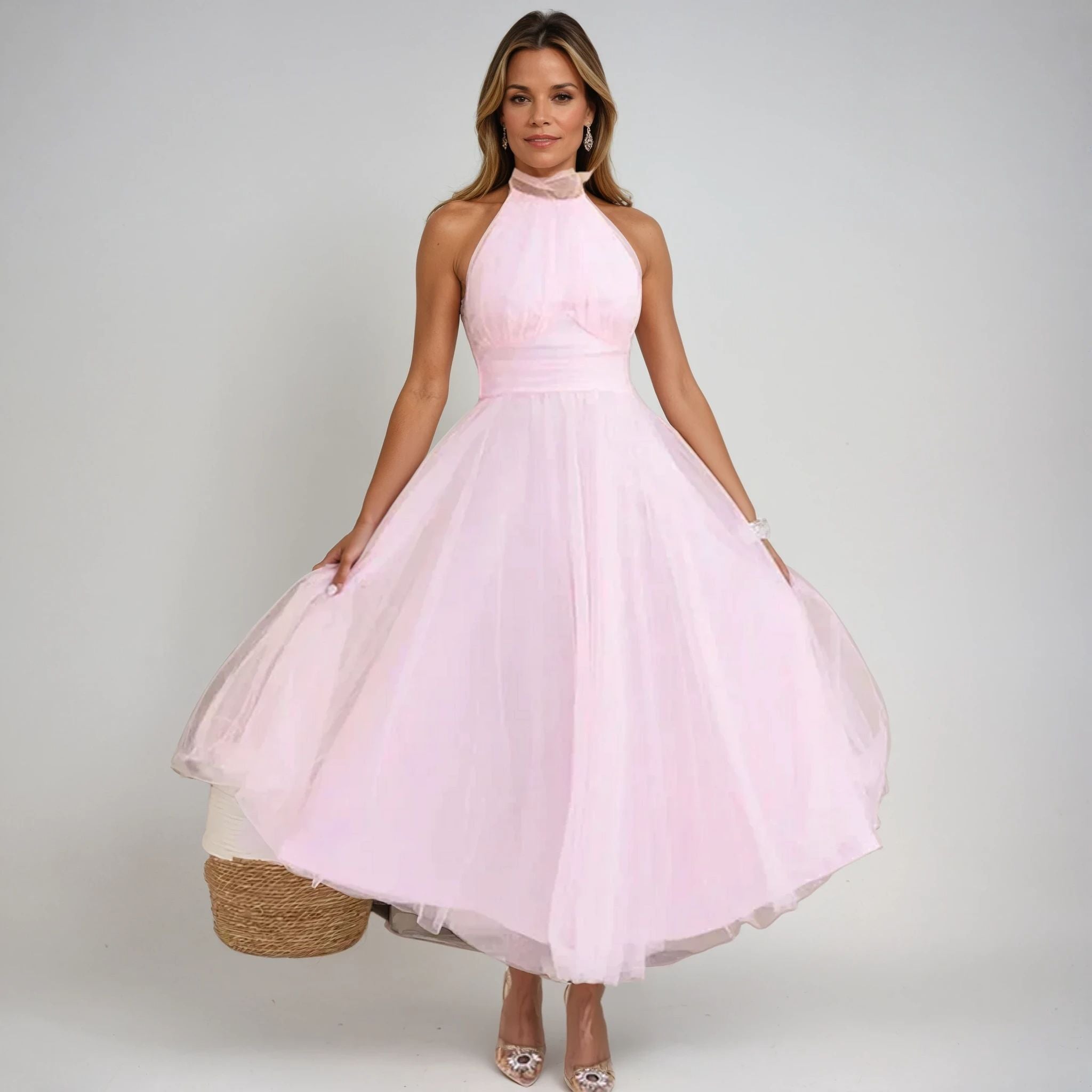 Kvinde i lyserød halterneck kjole, elegant design, poserer mod hvid baggrund. Perfekt til bryllup, fest eller formel begivenhed.