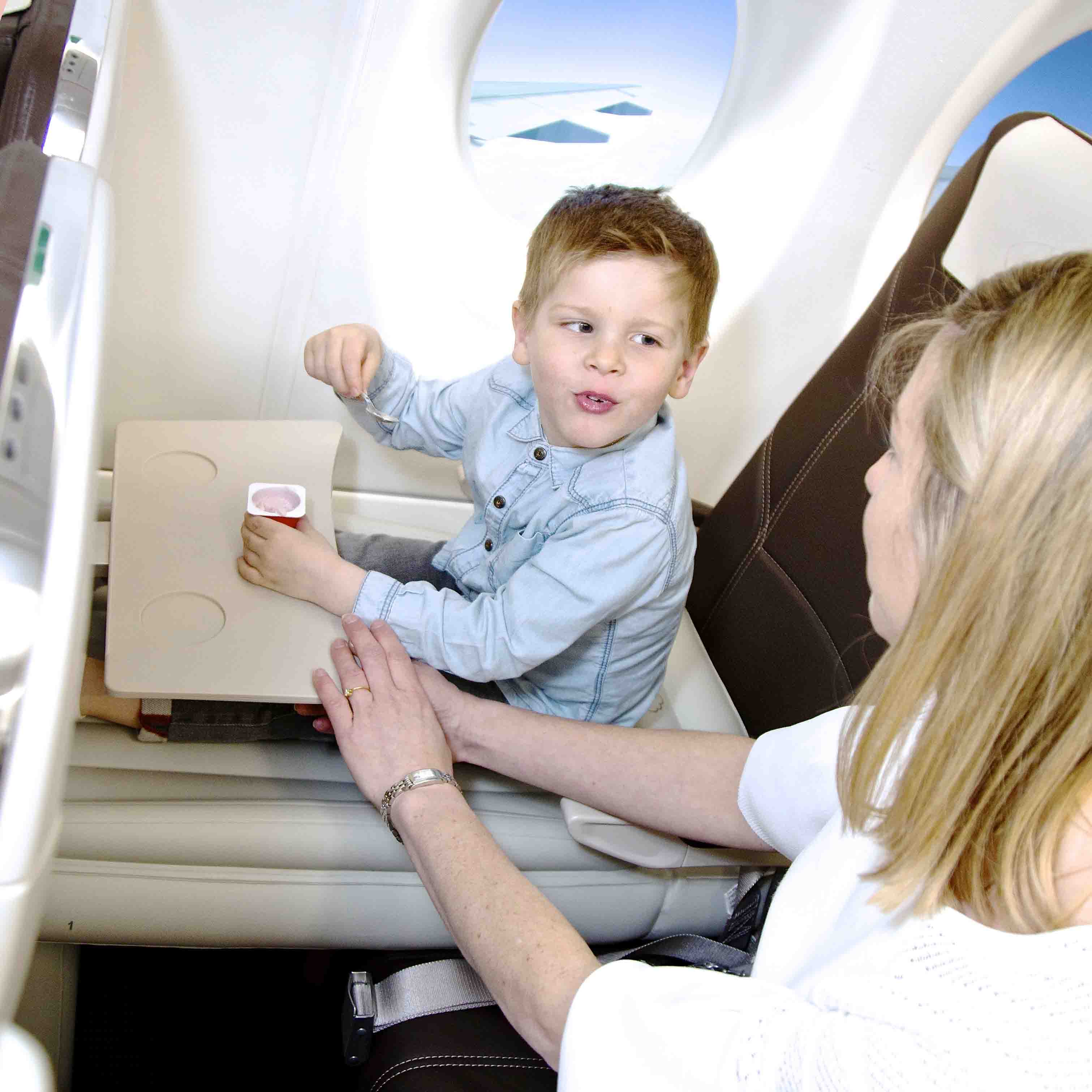 Dreng i flysæde med is, sidder ved siden af kvinde. Flyrejse, børnevenlig, komfortabel kabine, rejseoplevelse, familieferie, flyinteriør.