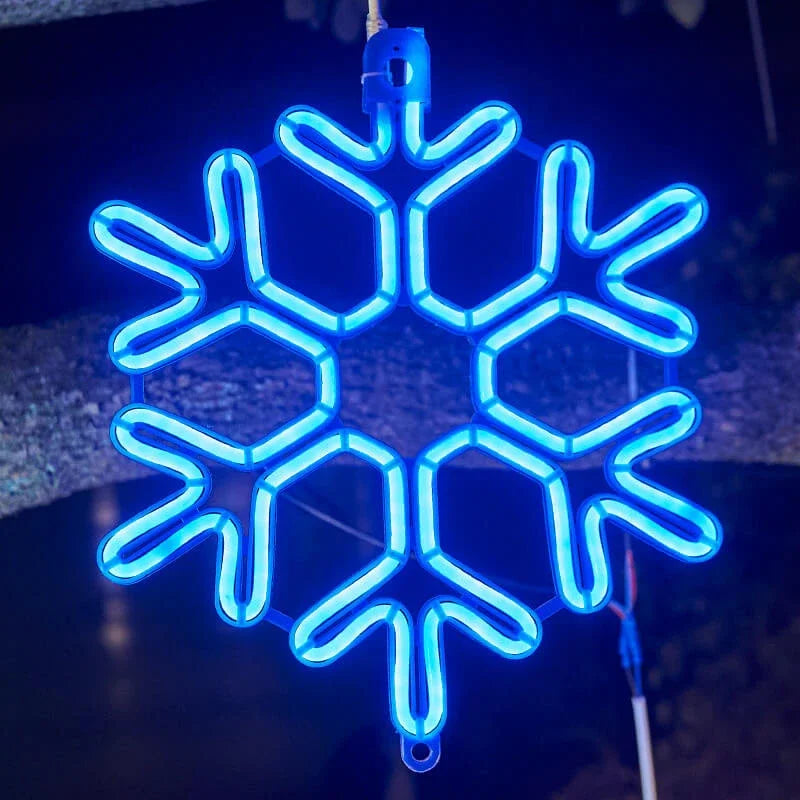 Blå neon snefnug lysdekoration hængende på træ, vinterbelysning, julepynt, udendørs LED snefnug, festlig stemning, natbelysning.