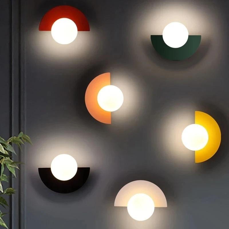 Væglamper i moderne design med halvcirkelformede farvede skærme og runde lyskilder på mørk væg. Stilfuld belysning, indretning, interiør.