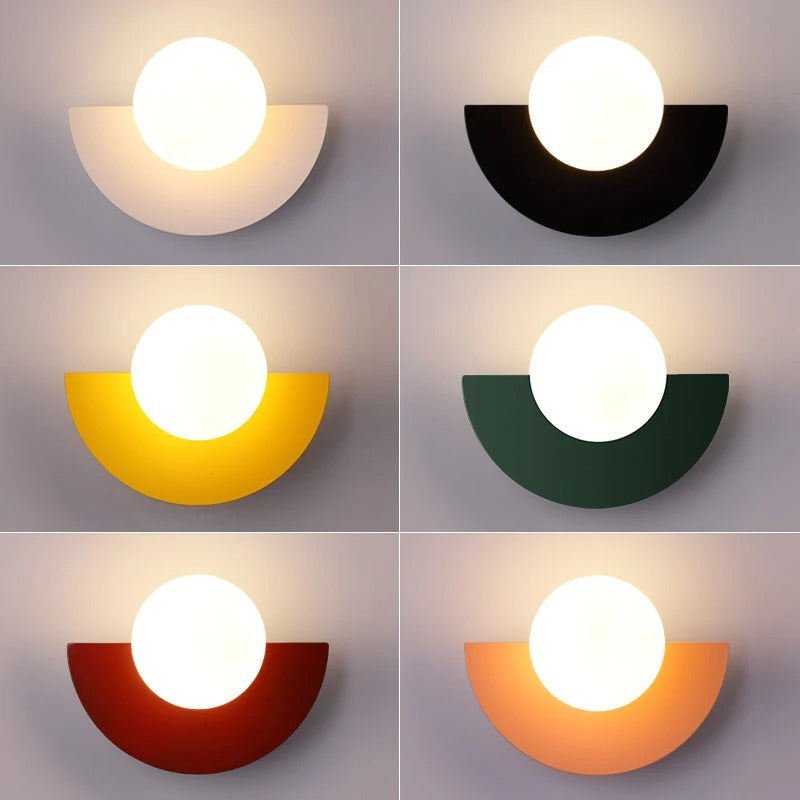 Seks moderne væglamper i forskellige farver: hvid, sort, gul, grøn, rød og orange. Halvcirkelformet design med rund lyskilde.