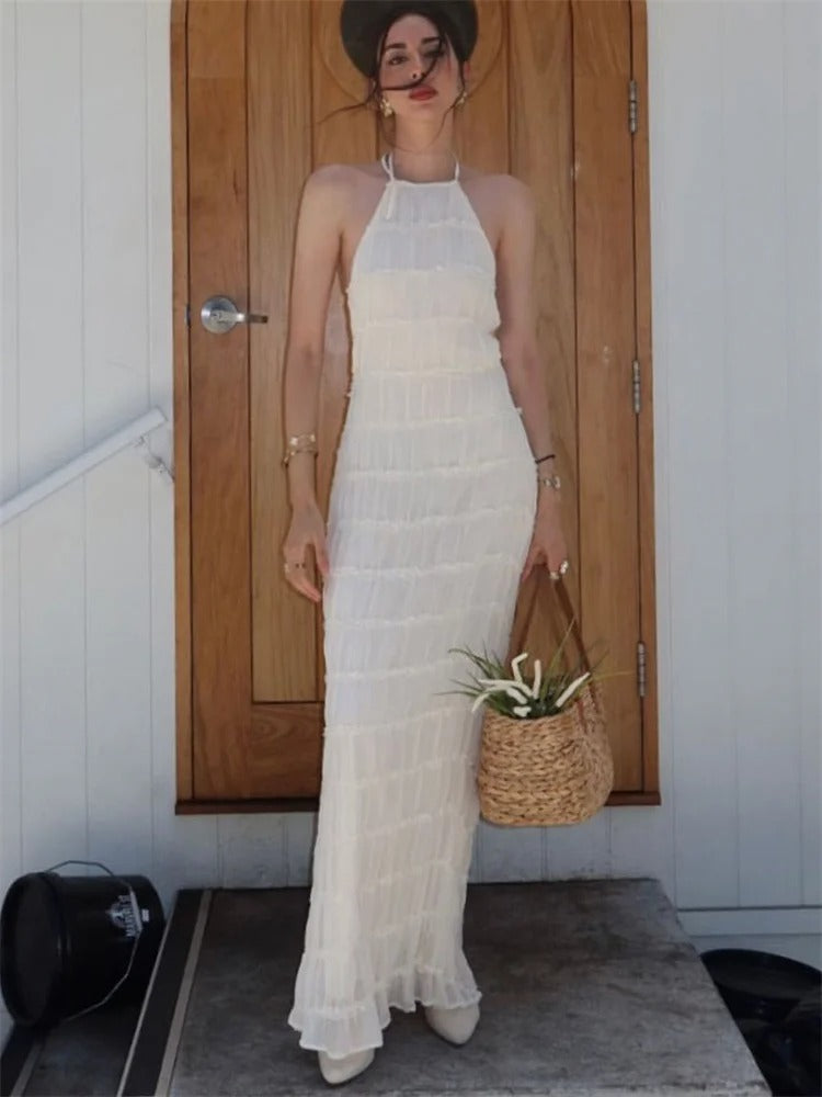 Kvinde i hvid sommerkjole foran trædør, holder flettet kurv. Elegant boho-stil, perfekt til sommermode.