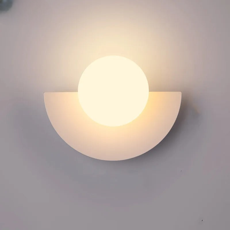 Væglampe i moderne design med halvcirkelformet base og rund lyskilde. Stilfuld belysning til hjemmet, ideel til stue eller soveværelse.