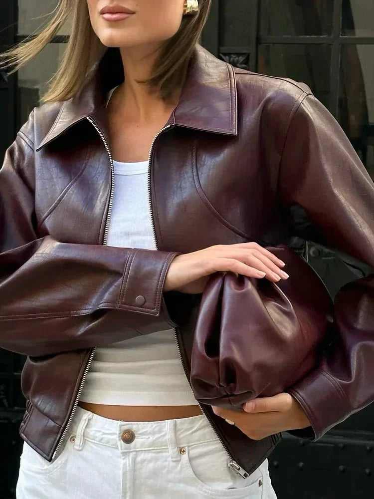 Kvinde iført brun læderjakke og hvid top, holder matchende brun lædertaske. Mode, stilfuldt outfit, læderjakke, trendy tilbehør.