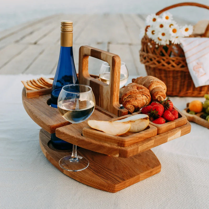Træserveringsbakke med vinflaske, vinglas, brød, jordbær og pærer på picnicbord. Perfekt til udendørs picnic og hygge.