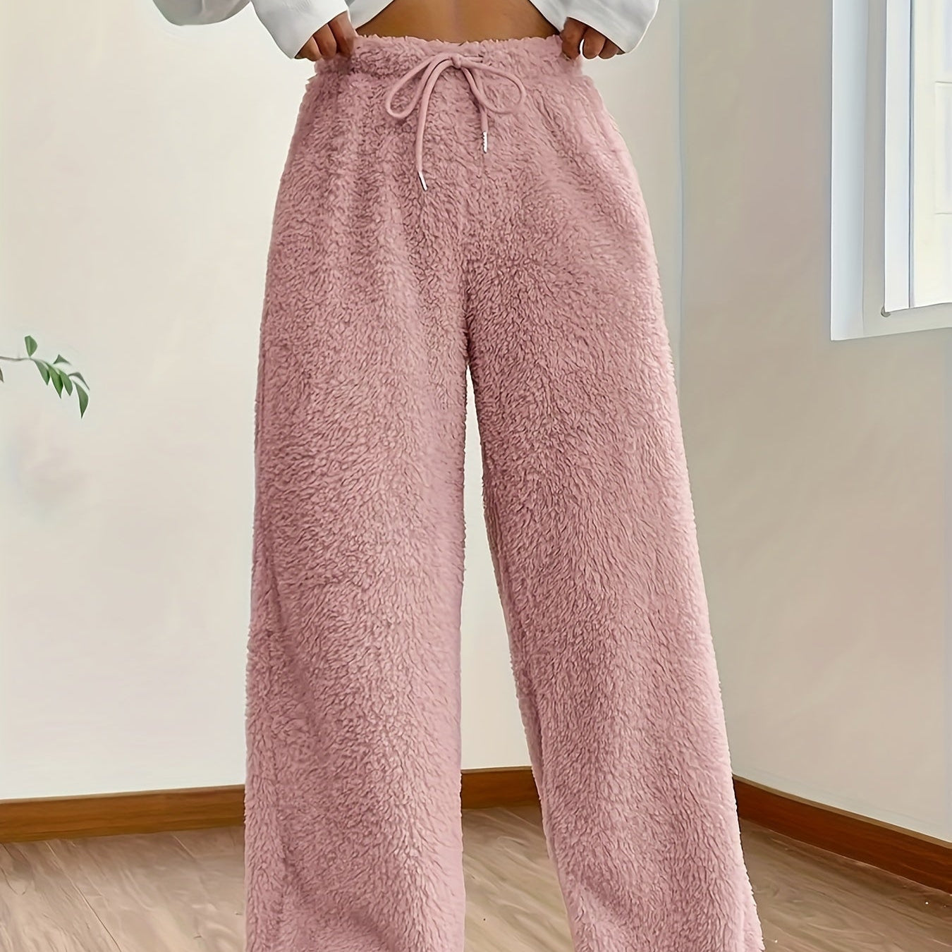 Kvinde iført lyserøde fleecebukser i stue. Komfortabelt, blødt materiale, perfekt til afslapning. Mode, hygge, hjemmetøj, trendy stil.